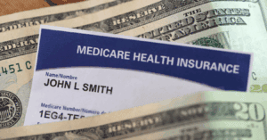 Basics of medicare. A medical insurance card is poking out through a number of 20 dollar notes, lying flat on a table. The medical insurance card reads "medicare health insurance" and is owned by fictional character, John L. Smith.